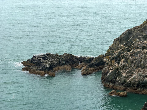 Jagged coastal rocks meet blue-green seawater along the rugged shoreline of the Howth Peninsula in County Dublin, Ireland.