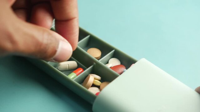 Close-up shot of a hand organizing colorful pills in a pill box, showcasing daily medication management and healthcare routine