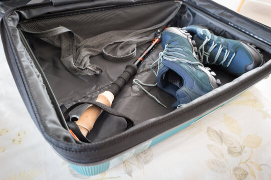 Opened hard shell suitcase showing a carbon fibre hiking pole and a pair of new, summer hiking shoes. Seen on a hotel bed soon after arriving.