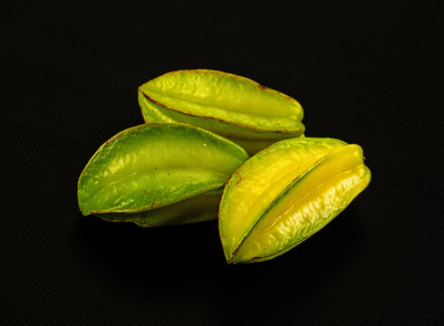Three starfruit slices in varying green and yellow tones on black textured background, close up with shallow depth of field