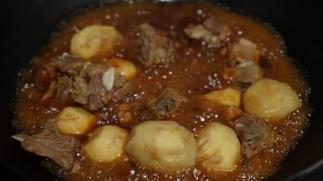 Taros or Chinese eddo&zwnj;es roasted pork ribs being stewed in an iron pot on the stove. Sichuan flavor style. Slow motion.