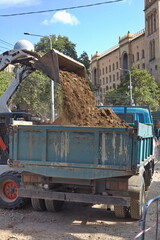 Compact loader dumping excavated soil and gravel into a dump truck during urban road reconstruction  © Анна Хмеленок