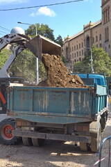 Compact loader dumping excavated soil and gravel into a dump truck during urban road reconstruction  © Анна Хмеленок