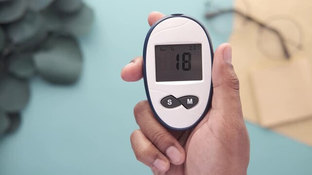Person holding blood glucose monitor showing digital reading during medical testing