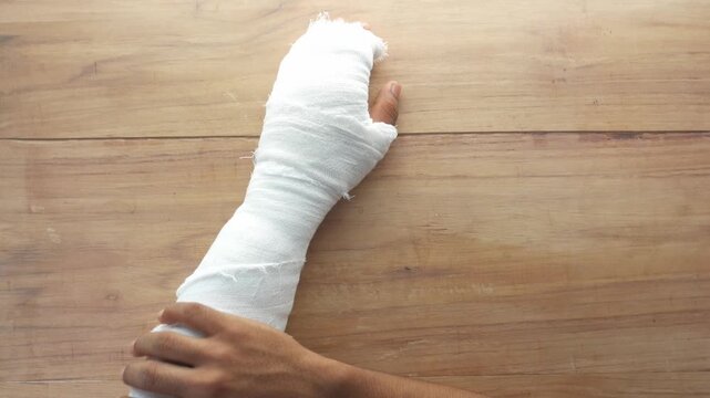Close up of a person's arm wrapped in a white medical bandage lying on a wooden table