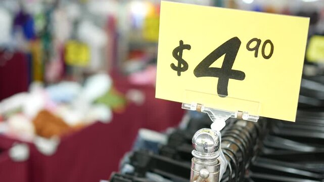 Close up of yellow price tag showing four dollars and ninety cents on clothing rack in retail store
