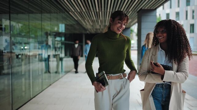 Two young female startup partners walking in a modern office building going to work. International business women