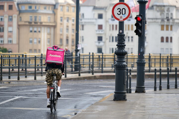 Fototapeta premium Foodora bicycle delivery courier riding along a city street next to traffic signs in Budapest, Hungary