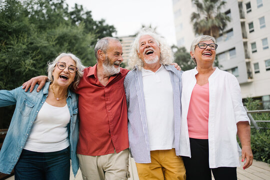 Happy senior friends bonding, walking and laughing together in city park enjoying active retirement