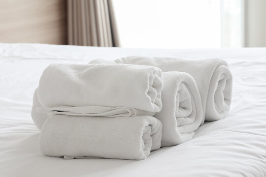 Rolled clean white cotton towels neatly stacked on a soft white bed sheet in a hotel room, symbolizing hospitality, spa relaxation, and luxury comfort.