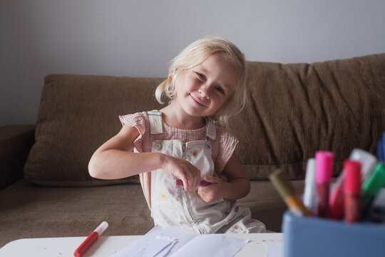 Focused little girl drawing with glitter pen at craft table at home