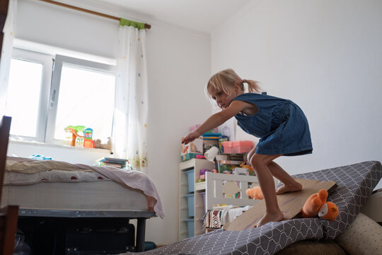  girl balancing on improvised slide from mattress and cardboard in bedroom
