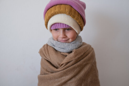  little girl wrapped in warm scarf wearing several knitted winter beanies