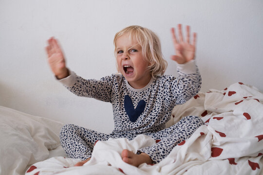 Angry little girl shouting and waving hands in bed throwing morning tantrum
