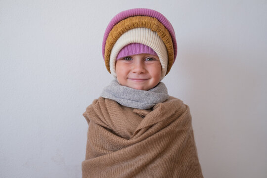  little girl wrapped in warm scarf wearing several knitted winter beanies