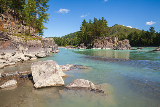 A turquoise mountain river winds around rugged rock cliffs and forested banks under a clear blue sky, evoking peaceful, adventurous outdoor feelings and pristine natural landscape scenery. Katun river