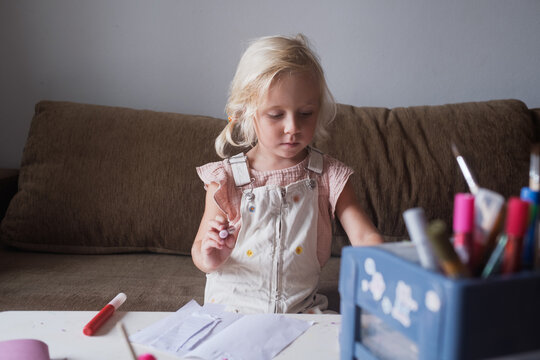 Focused little girl drawing with glitter pen at craft table at home