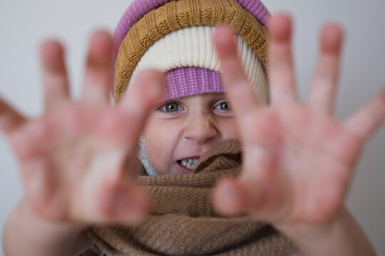  girl making scary face reaching hands towards camera in warm winter beanies