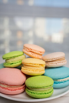close-up of a colorful stack of pastel macarons on a white plate by a sunlit window, with soft natural light, shallow depth-of-field, blurred urban background and an inviting delicate mood, detail