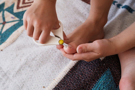 Child trimming toenails with safety scissors sitting on patterned rug
