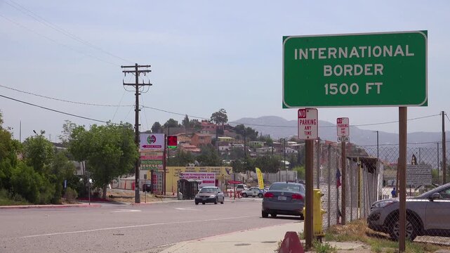 Roadside view of green international border sign near San Ysidro crossing and Tijuana hillside.