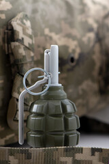 Military olive green grenade with visible safety pin and pull ring, against a blurred digital camouflage backdrop. Hand grenade f1 ideal for military, tactical gear, and safety-training content. © Hanna Aibetova