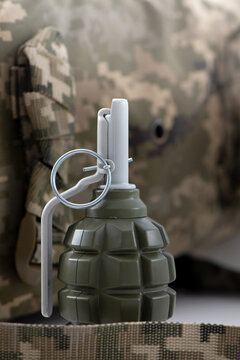 Military olive green grenade with visible safety pin and pull ring, against a blurred digital camouflage backdrop. Hand grenade f1 ideal for military, tactical gear, and safety-training content.