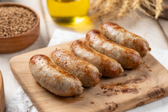 Juicy fried kupaty sausages served on a rustic wooden board with buckwheat and olive oil on table