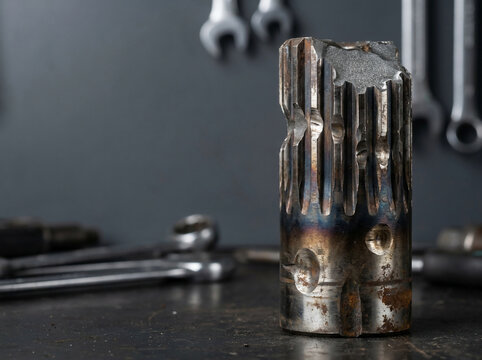 Closeup of a heavily worn and damaged industrial metal spline shaft with heat discoloration and surface pitting on a workshop workbench