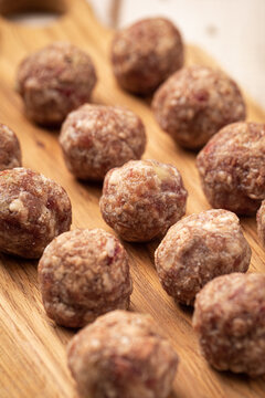 Uncooked minced beef meat balls for cooking on rustic wood board with herbs and tomatoes on white table