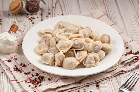 Traditional boiled meat pelmeni dumplings in white plate with spoons and napkin on wooden table top view