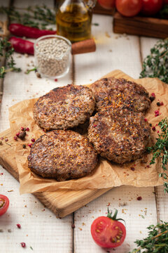 Grilled minced meat beef patties served on wooden cutting board with fresh herbs and spices on rustic table