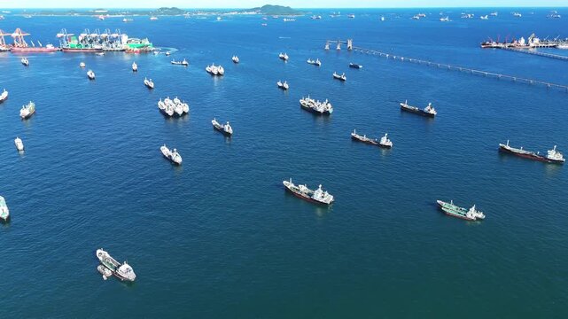 Fleet of oil tanker ships and commercial cargo vessels anchored in the deep blue sea near a long bridge. Global maritime logistics, international shipping trade, and energy transport.	