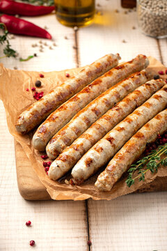 Fried grilled chicken meat sausages served with fresh thyme cherry tomatoes and pepper on wooden board
