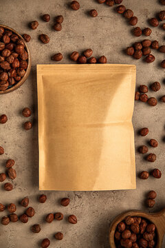 Standing blank kraft paper zipper pouch mockup surrounded by organic hazelnut nuts on stone table