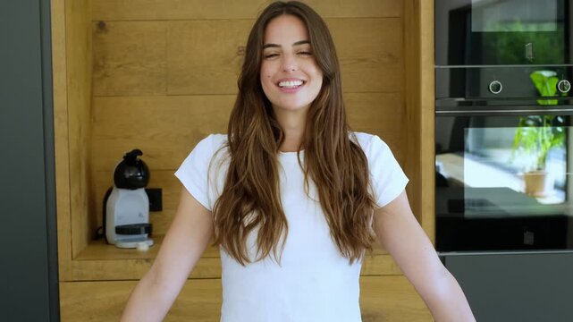 Portrait of an attractive and happy young woman smiling sincerely at the camera while standing in a modern kitchen, expressing genuine joy, contentment and positive emotions