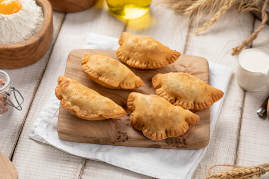 Crispy golden fried mini chebureki meat turnovers served on wooden cutting board with rustic ingredients