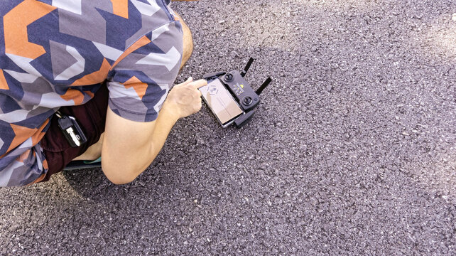 A person preparing and operating a compact camera drone on an asphalt road, with a remote controller and smartphone. Outdoor technology concept representing aerial photography