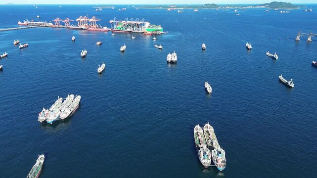 Fleet of oil tanker ships and commercial cargo vessels anchored in the deep blue sea near a long bridge. Global maritime logistics, international shipping trade, and energy transport.	