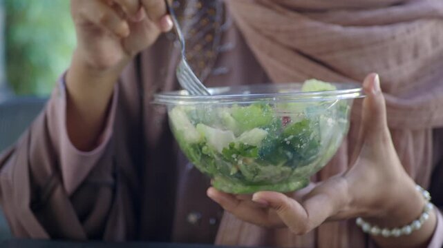 Close up motion of woman holding a bowl of fresh salad in a transparent bowl and eating in an outdoor setting