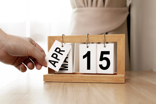 Hand changing wooden flip calendar to April 15. Concept of Tax Day deadline, tax return due date, event scheduling, and time management.