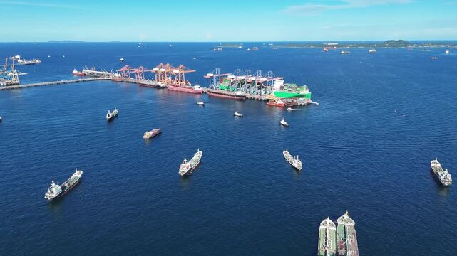 Fleet of oil tanker ships and commercial cargo vessels anchored in the deep blue sea near a long bridge. Global maritime logistics, international shipping trade, and energy transport.	