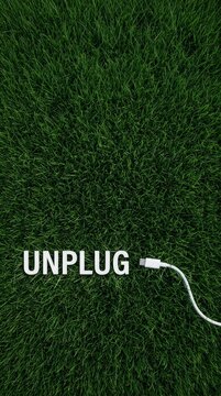 Charger lying on fresh green grass with the word 'UNPLUG,' symbolizing disconnecting.