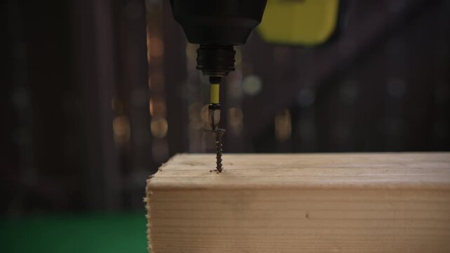 Driving screw into wooden surface using cordless drill close up showing fastening process and tool operation on wood