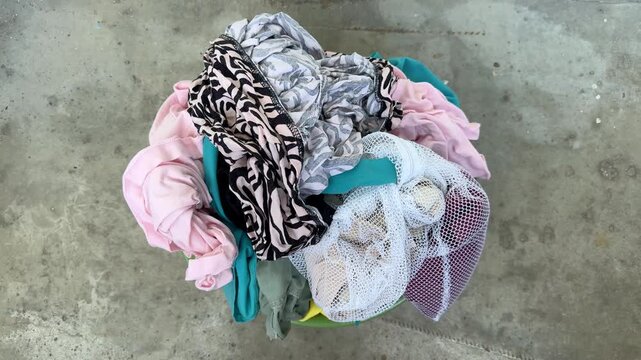 Clean laundry after washing on concrete floor, colorful wet clothes in basket ready for hanging and drying, household chore, fresh washed fabrics