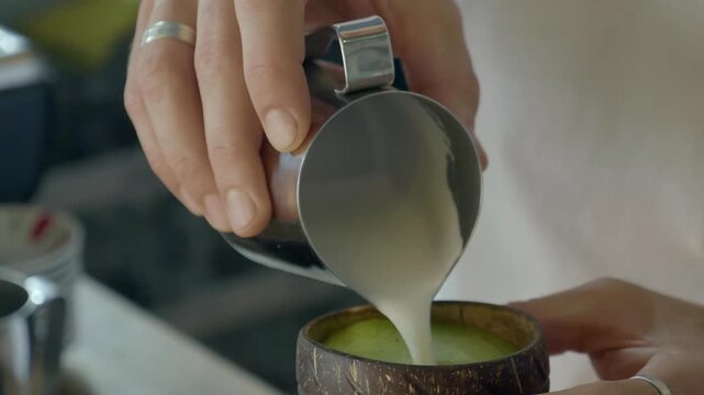 Close up shot of person pouring foamed milk into a mug made of coconut shell to make a matcha latte drink