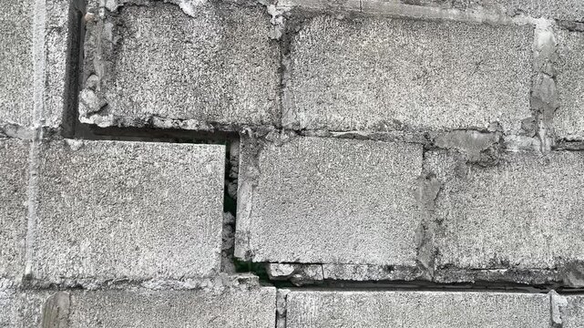 Cracked Concrete Block Wall: A close-up view of a weathered concrete block wall revealing significant cracks and damage, indicating structural weakness and wear.