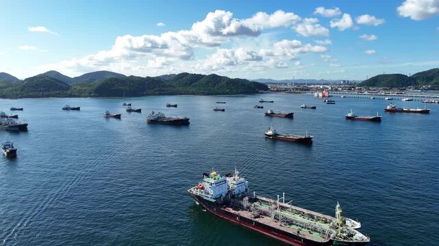 Fleet of oil tanker ships and commercial cargo vessels anchored in the deep blue sea near a long bridge. Global maritime logistics, international shipping trade, and energy transport.	