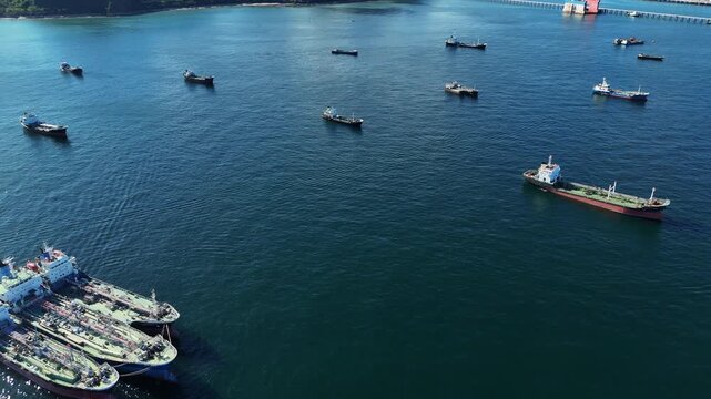 Fleet of oil tanker ships and commercial cargo vessels anchored in the deep blue sea near a long bridge. Global maritime logistics, international shipping trade, and energy transport.	