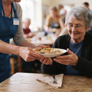 Caring volunteer serves a healthy meal to a smiling elderly woman in a community dining hall
